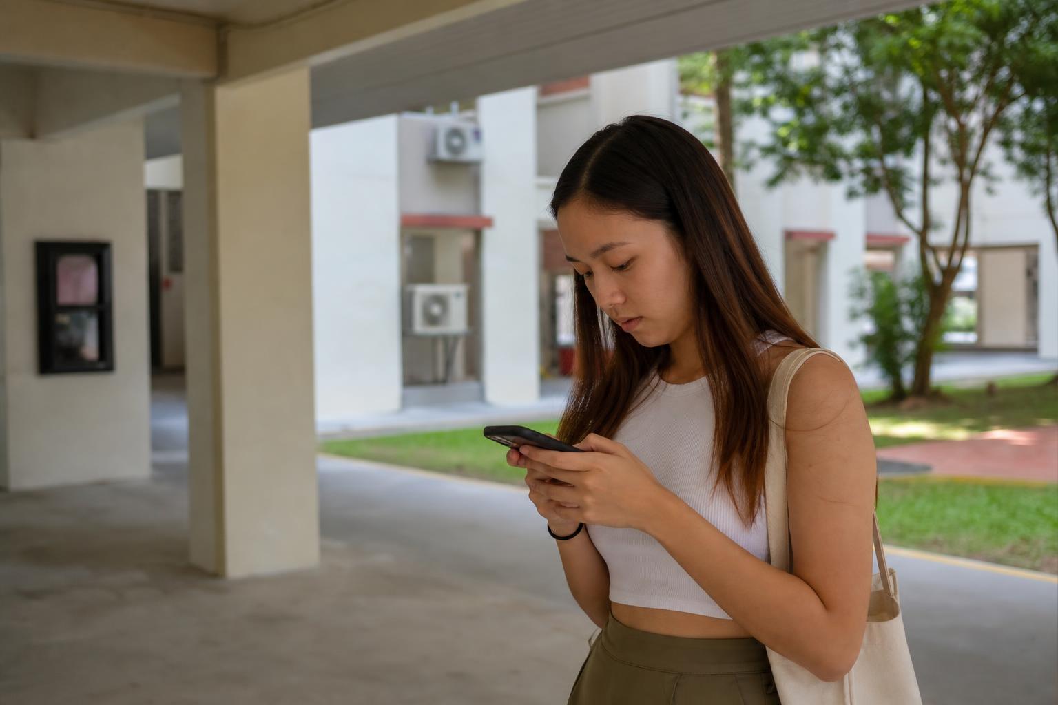 A young woman in a Singapore HDB estate searching for a service on her phone